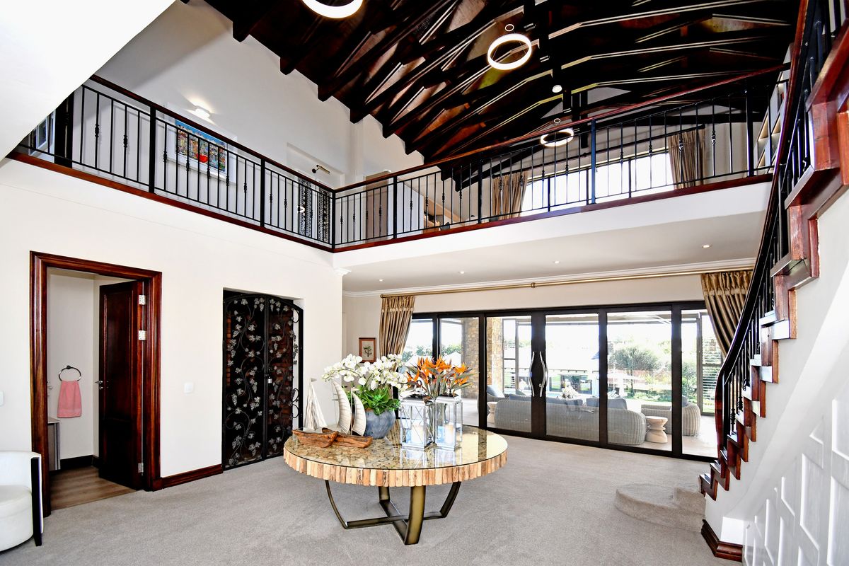 Spacious double-volume living area featuring a vaulted timber ceiling, mezzanine gallery with wrought iron railings, and large sliding doors leading to the patio.