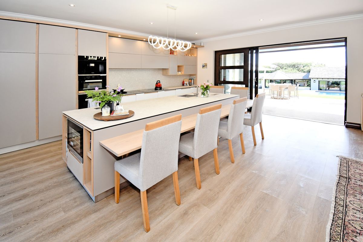 Modern open-plan kitchen featuring a large island with breakfast bar seating, high-end built-in appliances, and seamless access to the outdoor patio area.