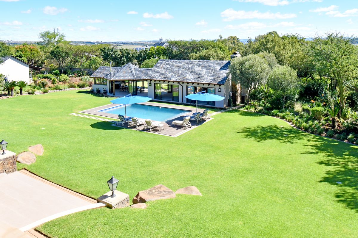 Aerial view of a well-maintained property featuring a swimming pool, timber decking, and expansive landscaped gardens.