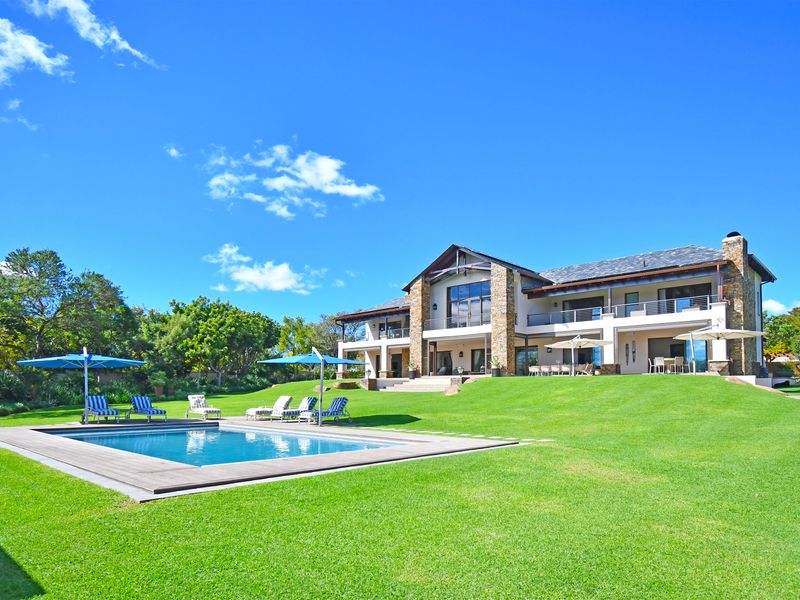 Spacious rear exterior view featuring a large landscaped lawn, a swimming pool with timber decking, and a multi-level residence with stone accents.