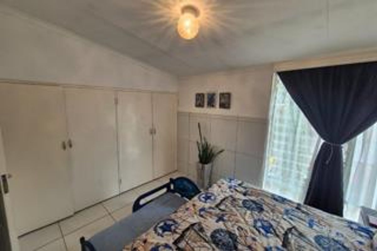 A bedroom featuring built-in floor-to-ceiling cabinetry, tiled flooring, and a large window with curtains providing natural light.