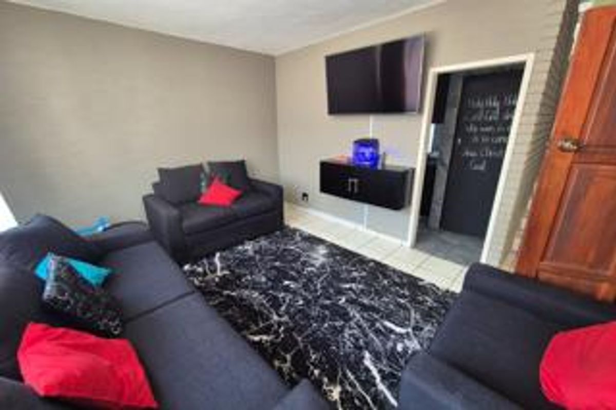 A living room featuring tiled flooring, a wall-mounted television, and a doorway leading to an adjacent space.