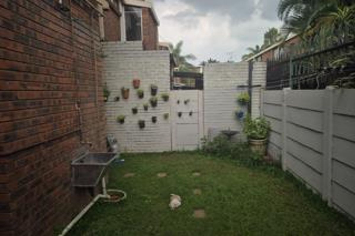 A private rear garden area featuring a brick facade, a wall-mounted utility sink, and perimeter boundary walls.