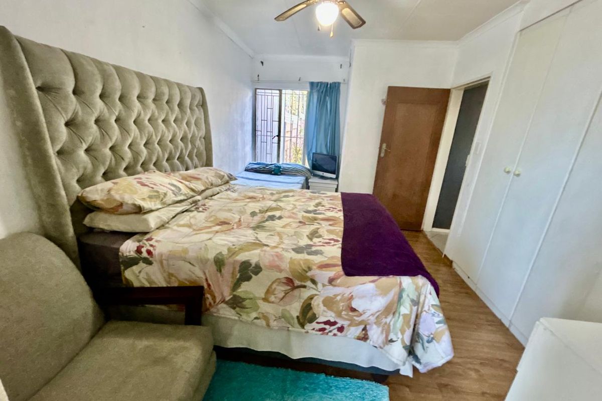 A functional bedroom featuring laminate flooring, built-in cupboards, and a ceiling fan, with a window fitted with a security gate.