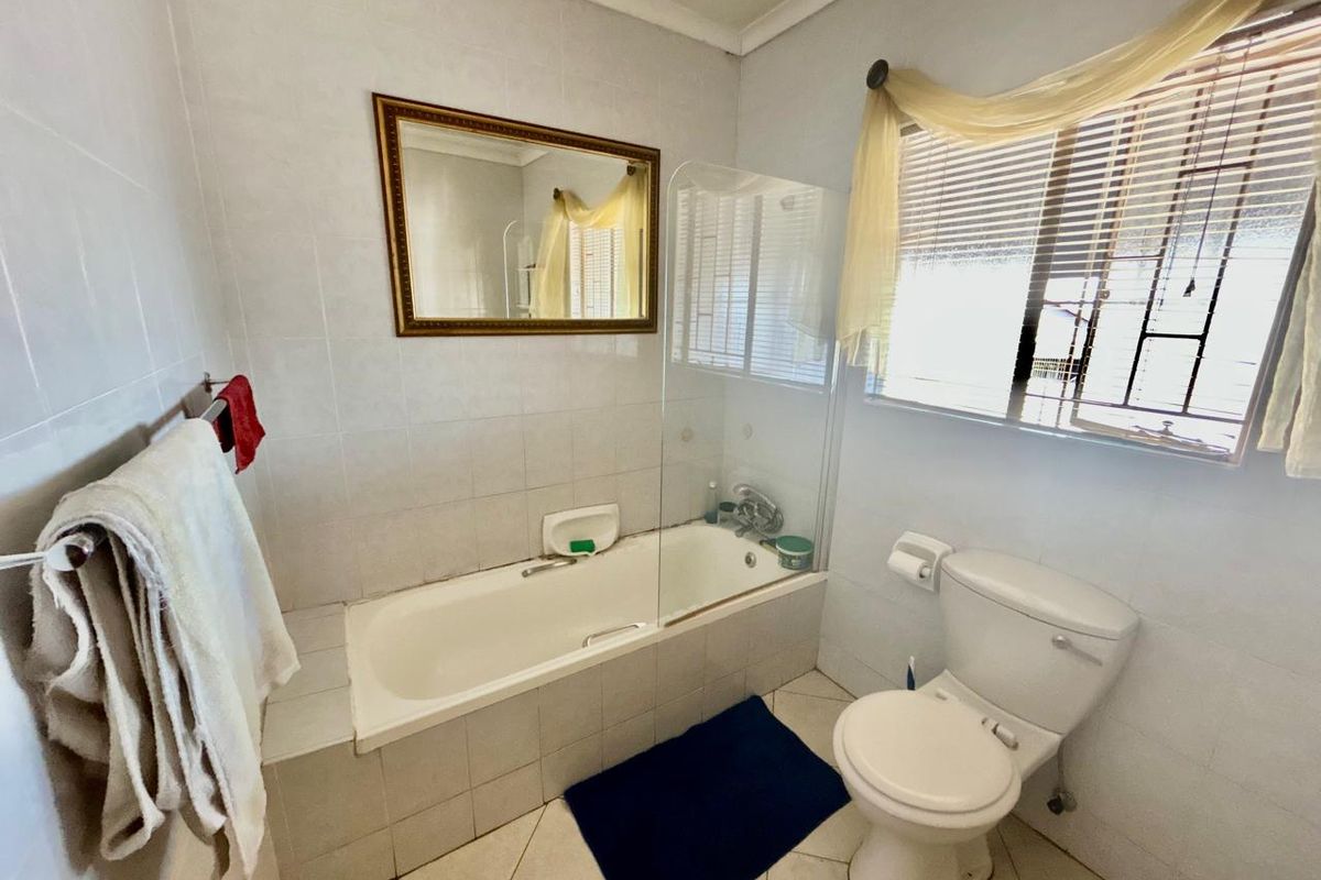 A functional bathroom featuring a built-in bathtub with a glass shower screen, tiled walls, and standard sanitary fixtures.