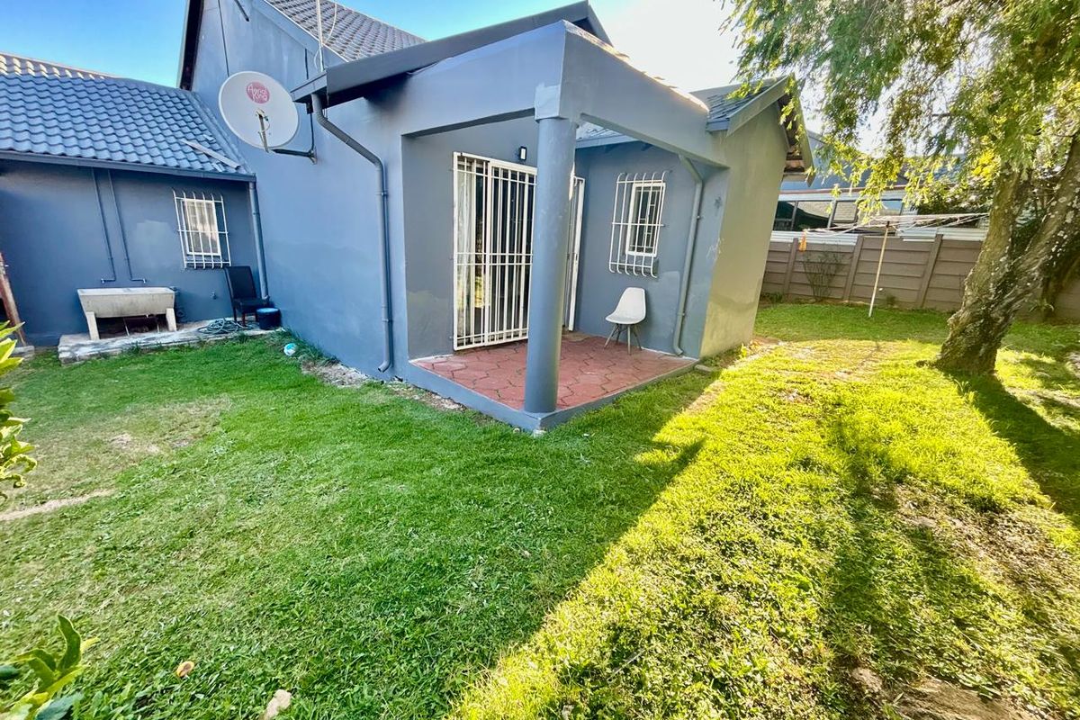 Rear view of the townhouse featuring a covered patio area, security gates, and a private garden space with a concrete laundry basin.