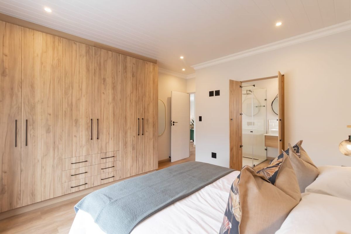 Modern bedroom featuring extensive built-in timber-look cabinetry, recessed lighting, and direct access to a private en-suite bathroom.