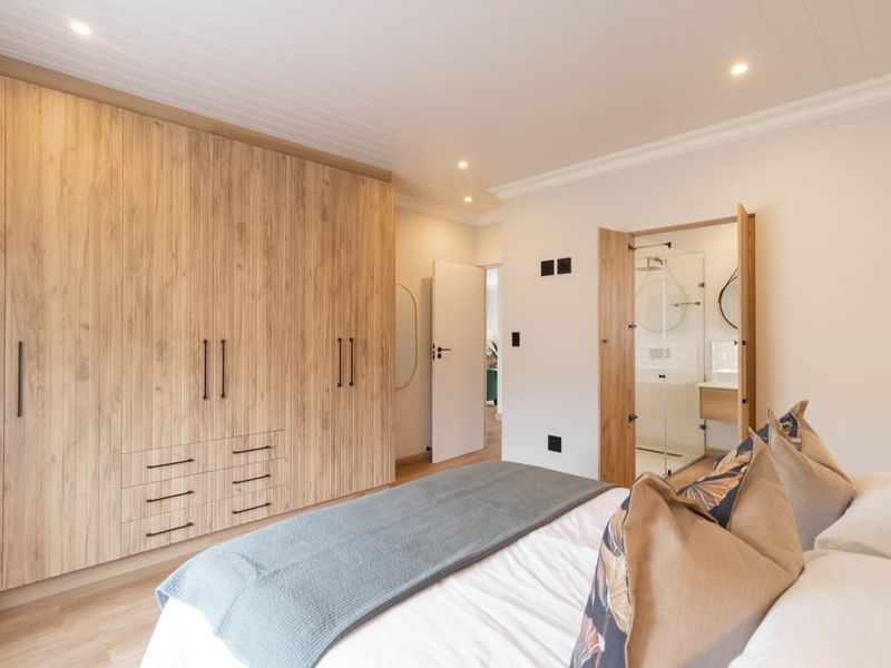 Modern bedroom featuring extensive built-in timber-look cabinetry, recessed lighting, and direct access to a private en-suite bathroom.