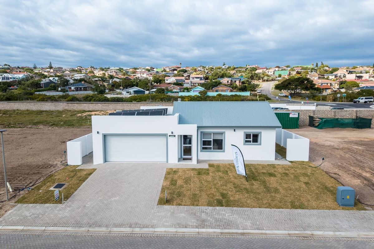Aerial view of a modern single-story house featuring a paved driveway, garage, solar panels, and a landscaped front lawn.
