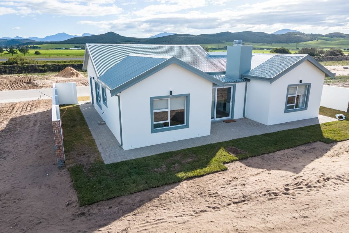 Aerial view of the rear elevation featuring a modern home with a corrugated metal roof, paved patio, and sliding glass doors set against a landscape.