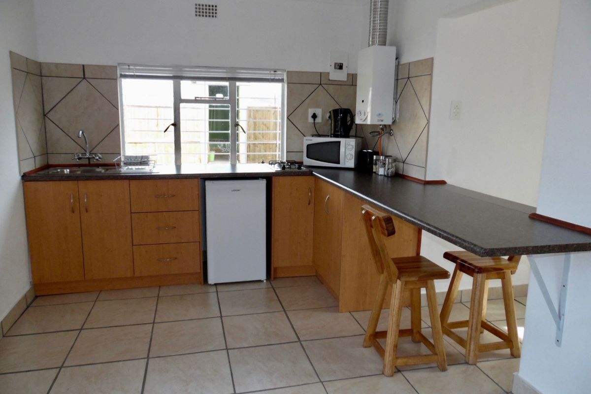 Functional kitchen featuring wooden cabinetry, tiled flooring, a breakfast bar, and a wall-mounted gas geyser.