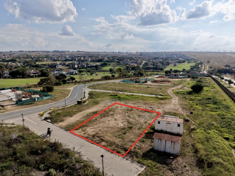 Aerial view of a vacant residential plot featuring a red boundary outline, situated in a developed estate with surrounding road infrastructure.