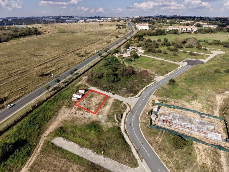 Aerial view of a vacant residential plot in a developing estate, featuring road access and proximity to local infrastructure.