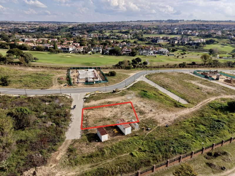 Aerial view of a vacant residential plot in a developed estate, featuring road access and surrounding landscape views.