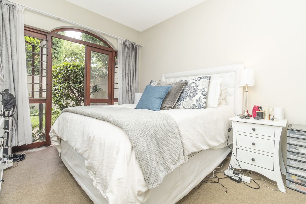 A well-lit bedroom featuring carpeted flooring and an arched timber-framed glass door providing direct access to the garden.