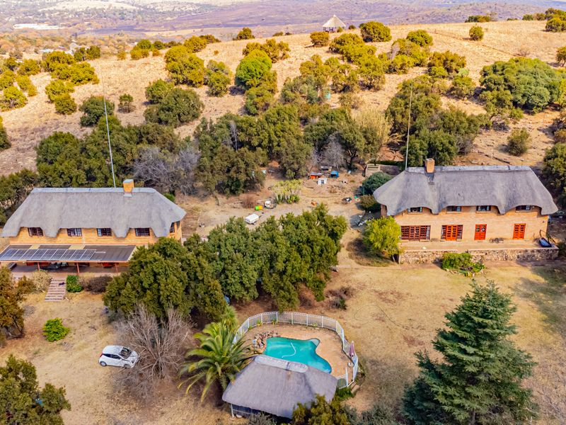 Aerial view of a small holding featuring two thatched-roof dwellings, a swimming pool, a thatched lapa, and expansive natural landscape.