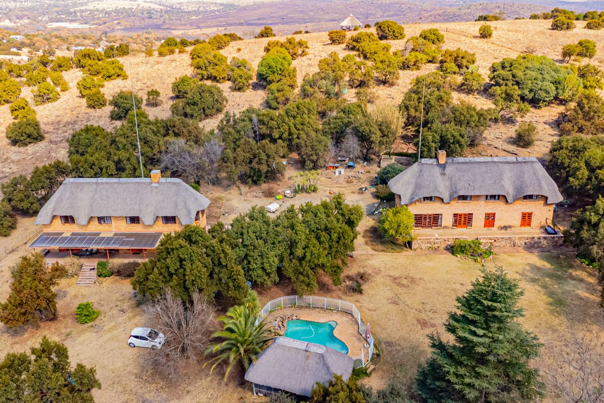 Aerial view of a small holding featuring two thatched-roof dwellings, a swimming pool, a thatched lapa, and expansive natural landscape.