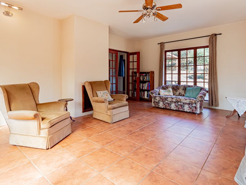 Spacious living room featuring terracotta floor tiles, a ceiling fan, and large windows with garden views, providing a bright and functional living space.