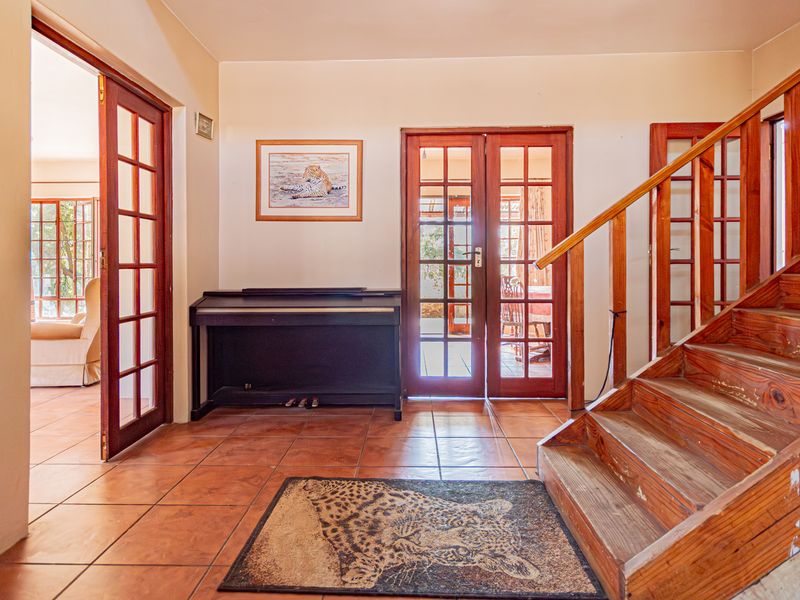 Welcoming entrance hall featuring terracotta floor tiles, a wooden staircase with a handrail, and multiple sets of classic wooden french doors.