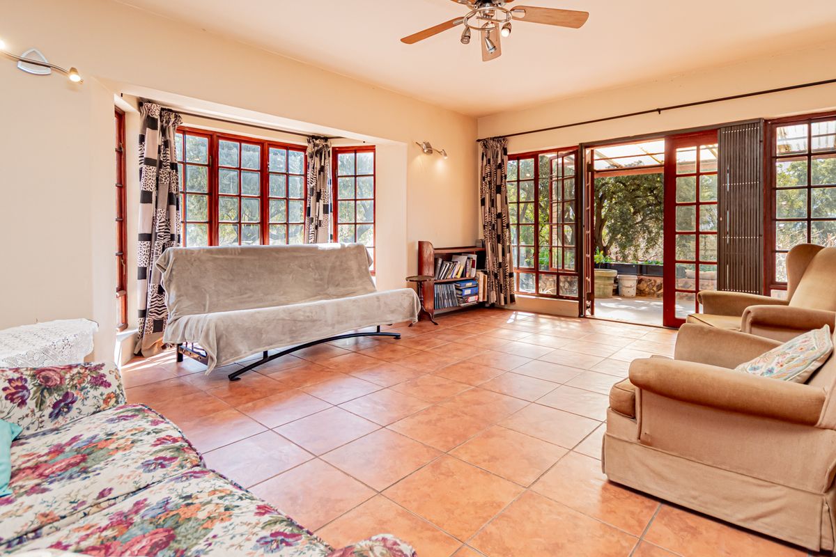 Spacious living room featuring terracotta-style tiled flooring, large wooden-framed windows, and direct access to an outdoor patio area.