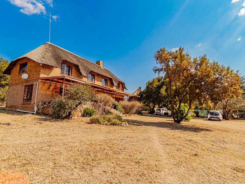 A view of the front elevation of a facebrick small holding property featuring a traditional thatch roof and a covered patio area.