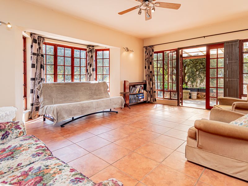 Spacious living room featuring terracotta-style tiled flooring, large wooden-framed windows, and direct access to an outdoor patio area.
