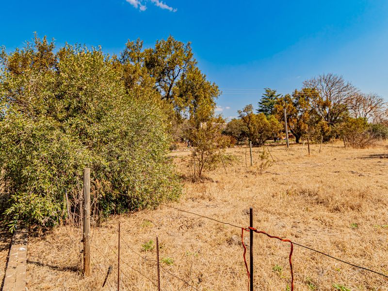 An expansive, undeveloped plot of land featuring dry grass, mature trees, and basic wire perimeter fencing.