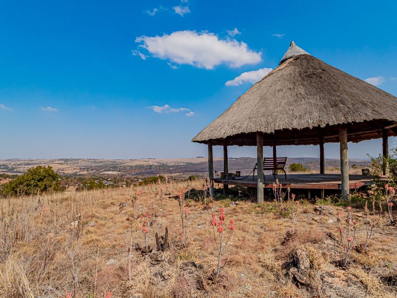 An open-air thatched gazebo structure featuring timber decking, offering panoramic views over the surrounding small holding landscape.