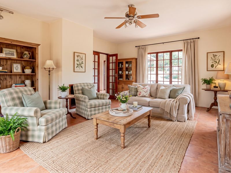 A well-maintained living room featuring terracotta floor tiles, a ceiling fan, and classic wooden window frames with french doors leading to adjacent spaces.