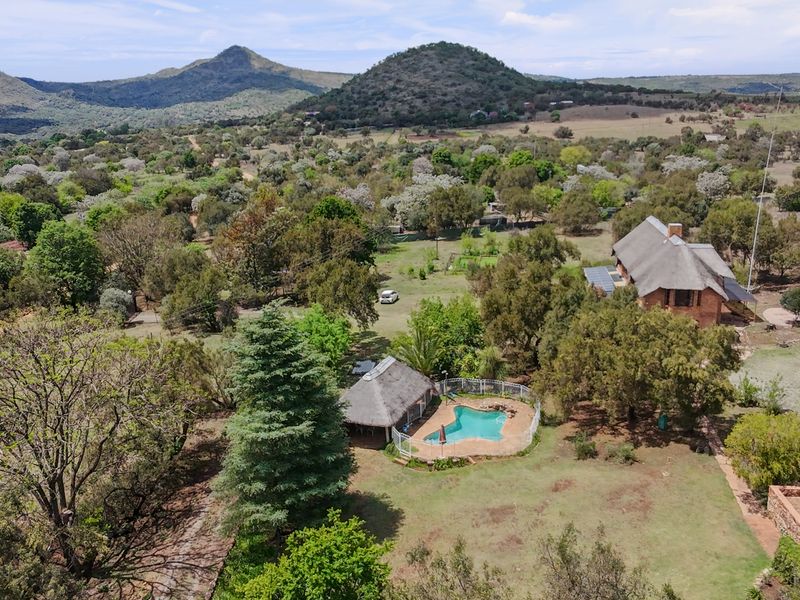 Aerial view of a small holding property featuring a swimming pool, thatched roof buildings, and expansive natural landscape with mountain views.