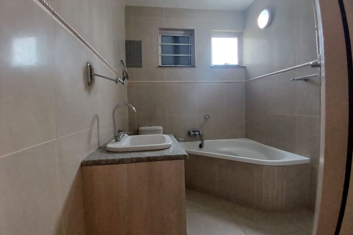 A functional bathroom featuring a corner bathtub, vanity cabinet with a countertop basin, and neutral wall tiling.