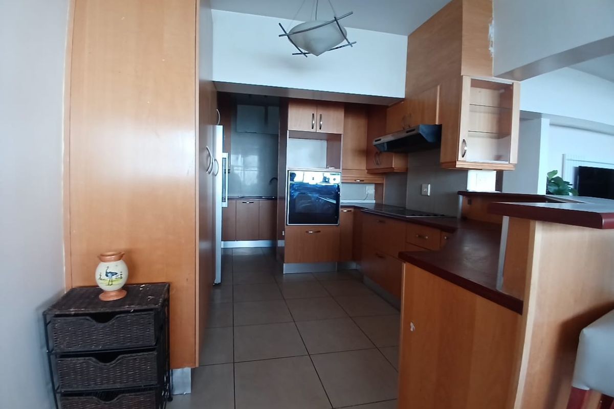 A functional kitchen featuring wood-finish cabinetry, built-in oven, extractor fan, and a breakfast bar, with tiled flooring throughout.