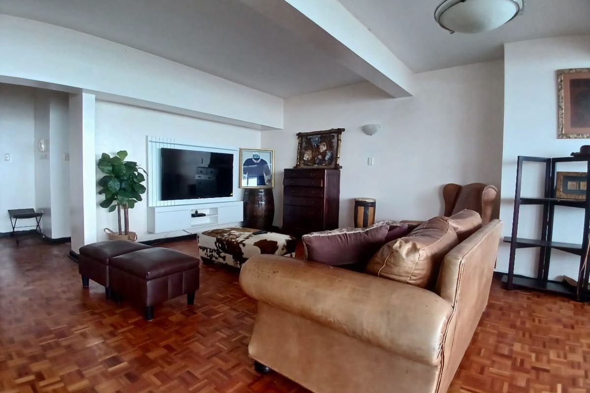 Spacious living room featuring classic parquet flooring, a built-in media console, and a prominent ceiling beam, offering a comfortable and functional layout.