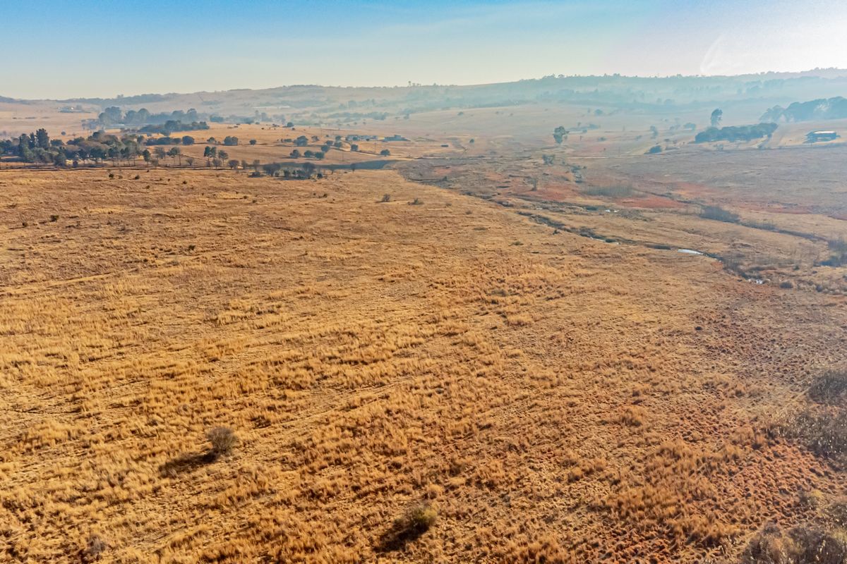 An aerial view of a large, open residential vacant land plot featuring natural grassland and a small watercourse running through the landscape.