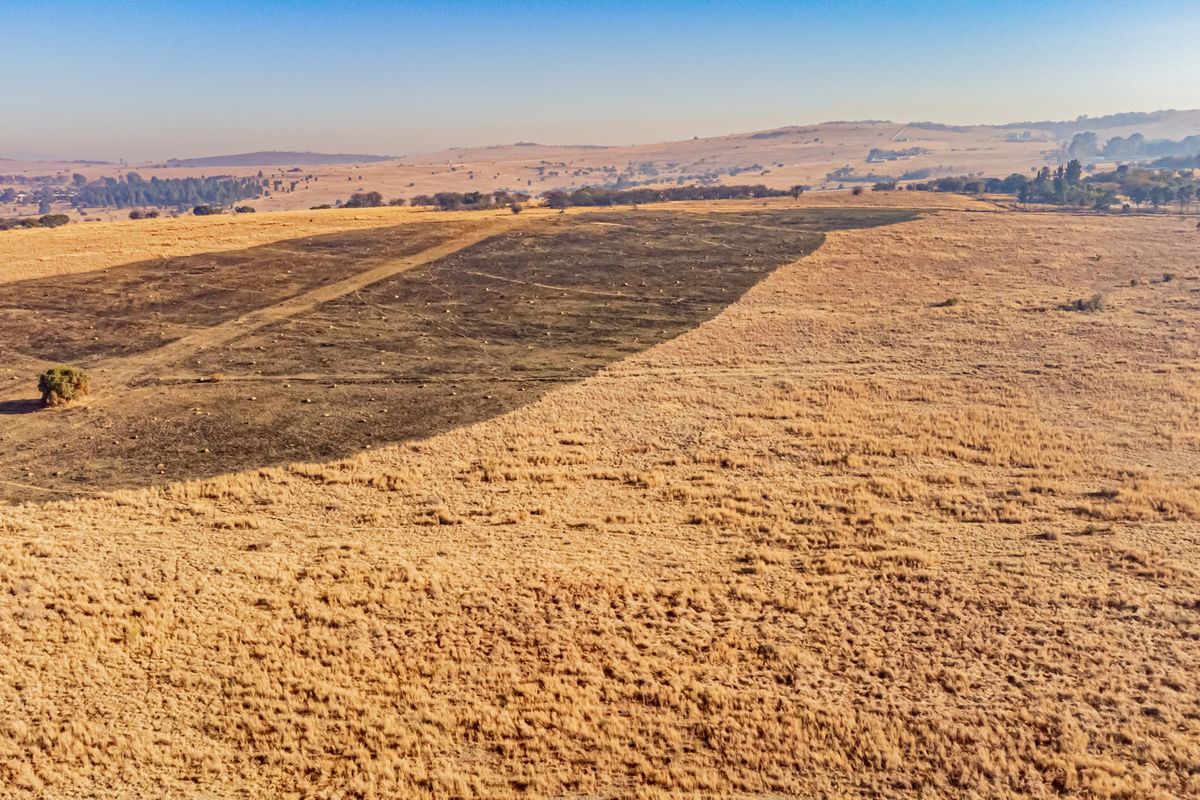 An aerial view of a large, open vacant residential land plot featuring dry grassland and a section of cleared terrain.