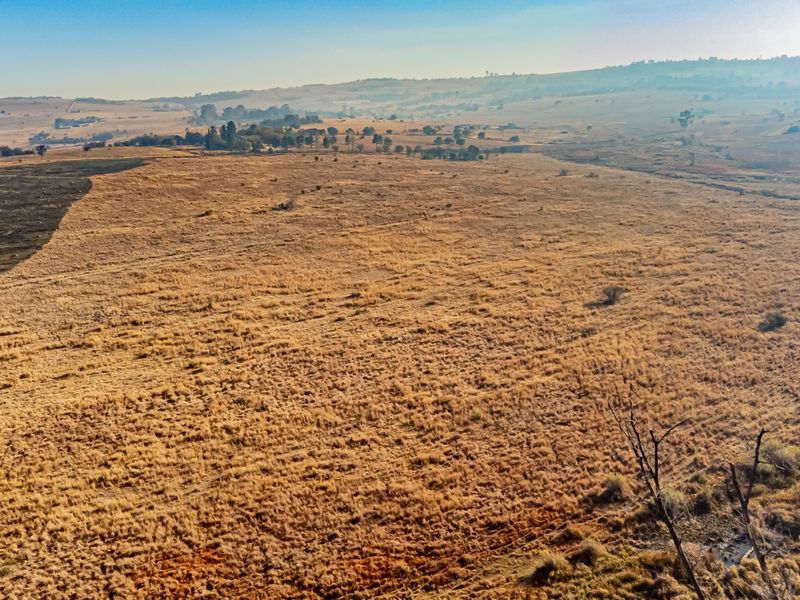 An aerial view of a large, undeveloped residential land plot featuring natural dry grassland and open terrain.