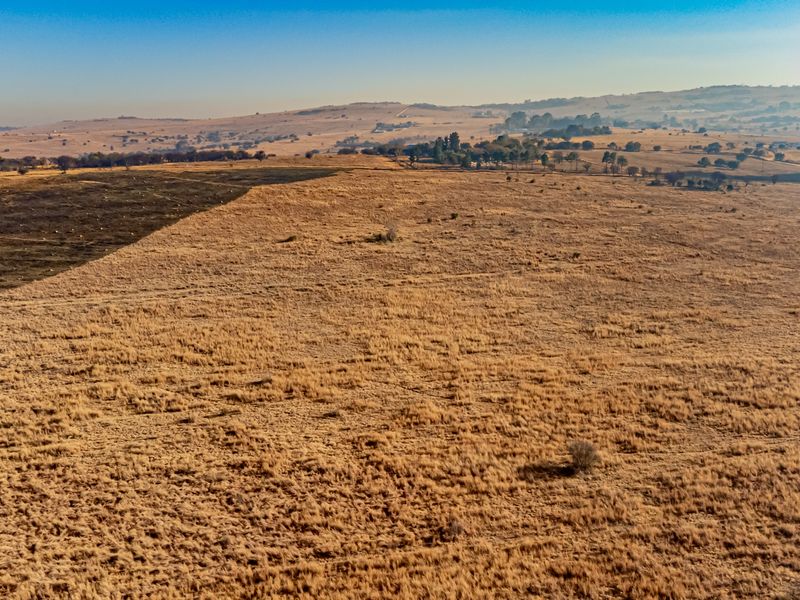 An aerial view of a large, undeveloped residential land parcel featuring dry grassland and rolling hills in the distance.
