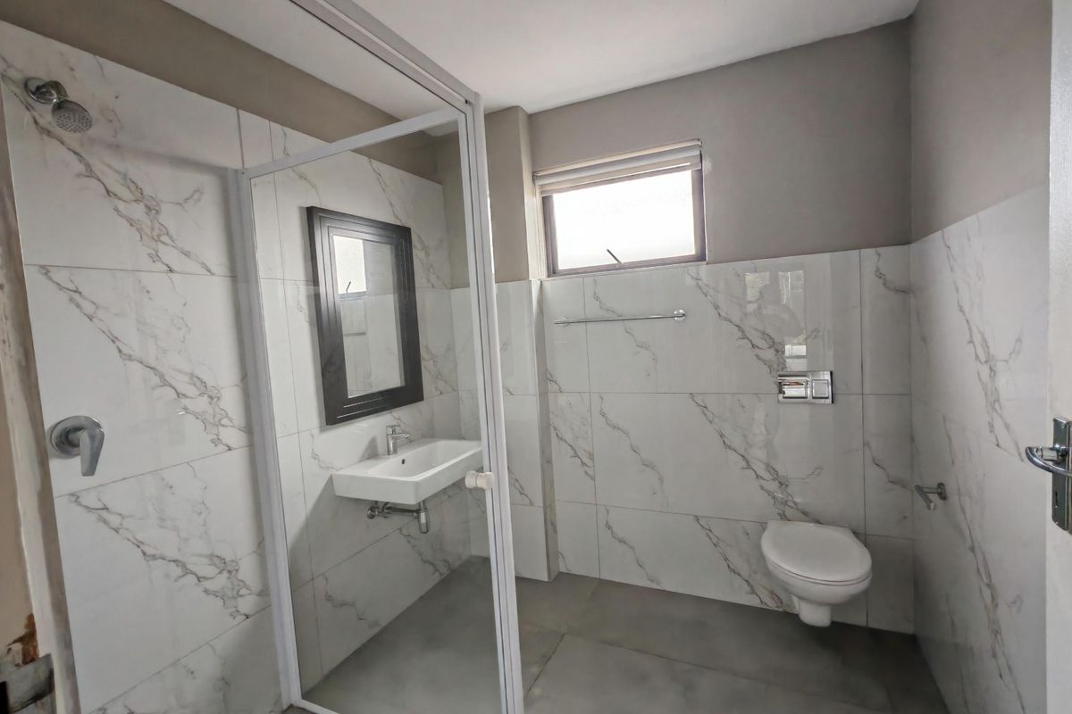 Modern bathroom featuring marble-look wall tiles, a glass-enclosed shower, wall-mounted basin, and a wall-hung toilet.