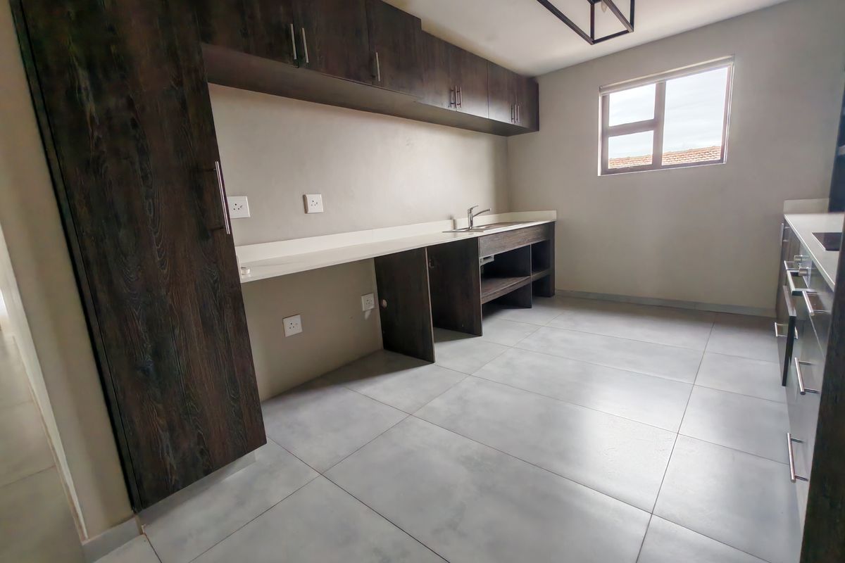 A modern kitchen featuring dark wood-grain cabinetry, stone countertops, a stainless steel sink, and large format floor tiles.