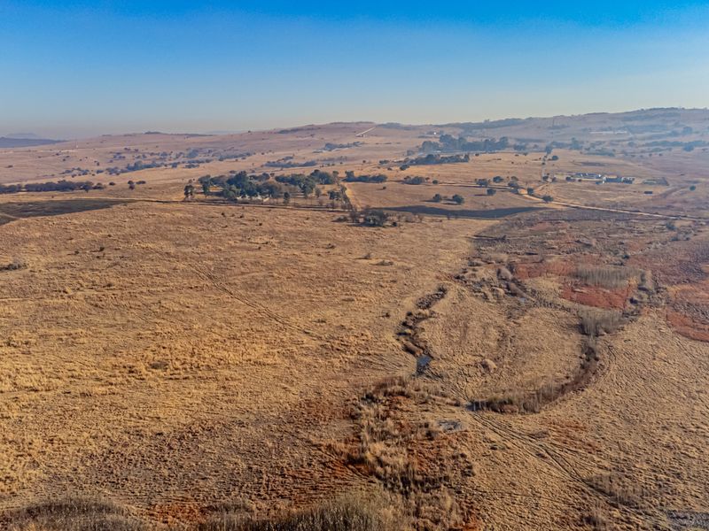 An expansive aerial view of open, undeveloped grassland featuring natural terrain and a winding watercourse, showcasing the property's vast landscape potential.