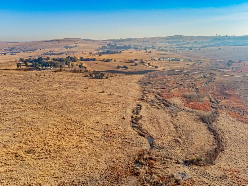 An aerial view of expansive, undeveloped residential land featuring natural grassland and a drainage line under a clear sky.
