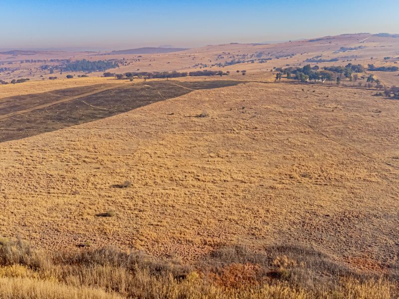 An aerial view of a large, open residential vacant land plot featuring dry grassland and rolling hills in the distance.