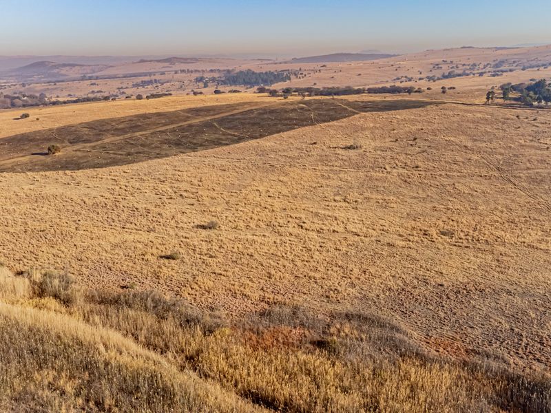 An aerial view of a large, open residential vacant land plot featuring dry grassland and rolling hills in the distance.