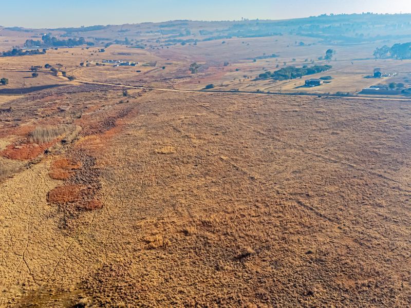 An aerial view of a large, undeveloped residential plot featuring natural grassland and expansive rural landscape views.