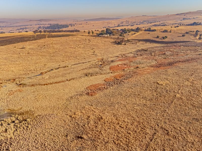 An aerial view of expansive, undeveloped residential land featuring natural terrain and open fields.