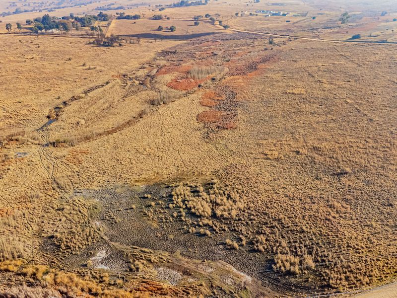 An aerial view of a large, undeveloped residential land parcel featuring natural grassland and a natural drainage line.