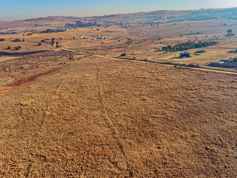 An aerial view of a large, undeveloped residential plot of land featuring dry grassland and surrounding rural landscape.