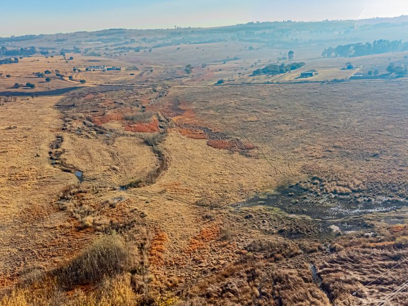 An aerial view of a large, open residential vacant land plot featuring natural grassland and a small watercourse.
