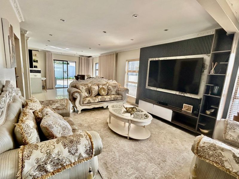 Spacious open-plan living area featuring a modern slatted feature wall with integrated media unit, recessed lighting, and seamless flow to the outdoor patio.