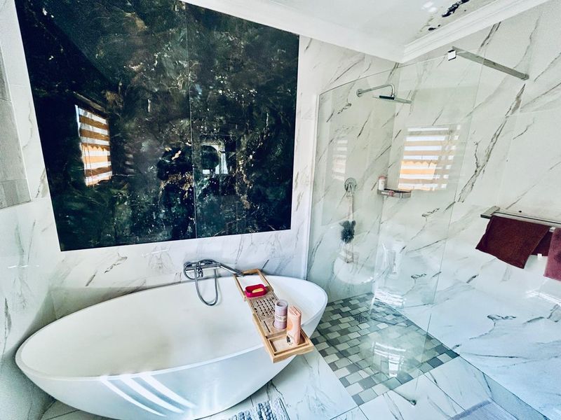 Modern bathroom featuring a freestanding bathtub, walk-in shower with glass screen, and marble-look tiling. Note visible water damage on the ceiling.